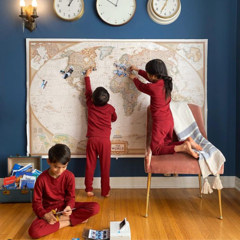 Three children wearing royal cherry merino wool base layers, playing with a map on a wall.
