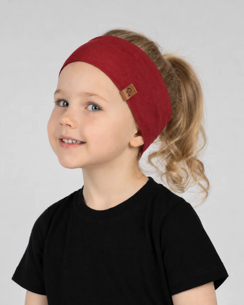 A smiling young girl with blonde hair tied in a ponytail, wearing a wide dark red headband with a small logo patch on the side and a black short-sleeved t-shirt, against a light gray background.