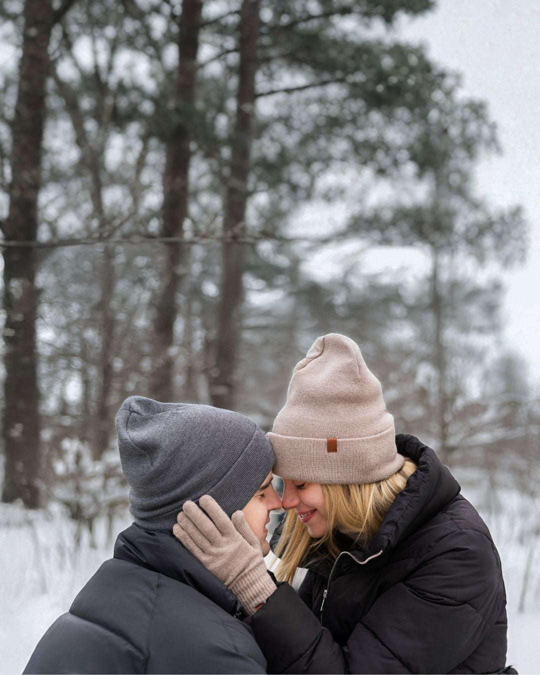 Two people in winter clothing embracing in a snowy forest.