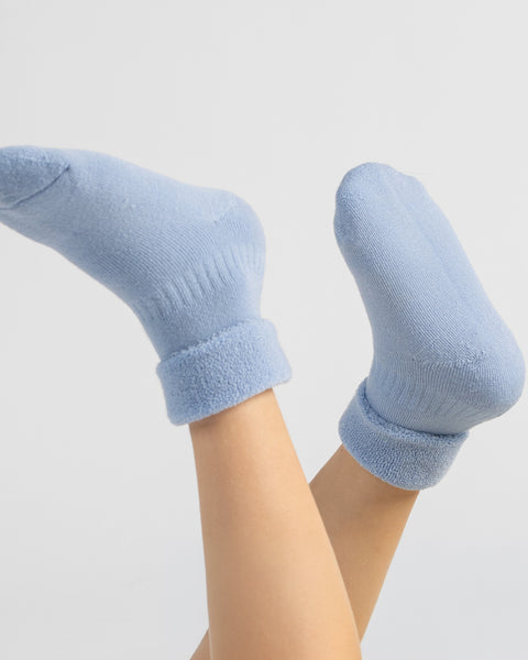 Close-up of a child's legs raised in the air wearing cozy, light blue knit ankle socks with folded cuffs.