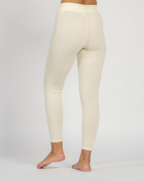 Close-up back view from the waist down of a person standing barefoot, wearing natural cream-colored leggings.