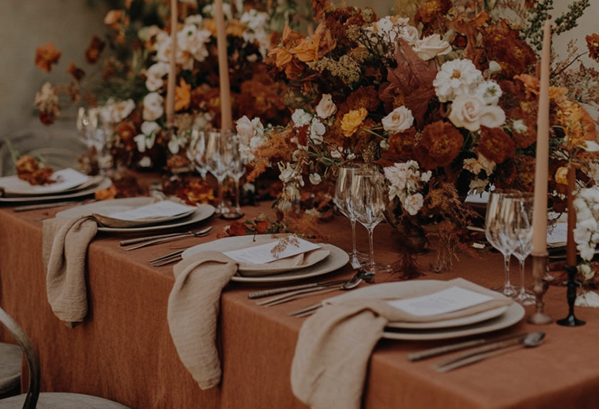 Decorative table setting with flowers, plates, and glasses on a brown tablecloth.