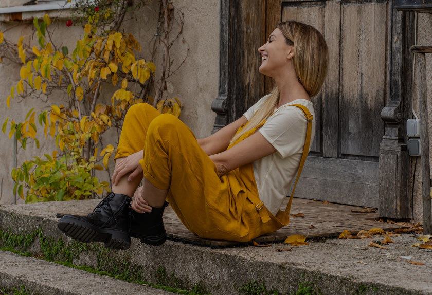Woman sitting on steps outdoors with a wooden door and yellow leaves in the background