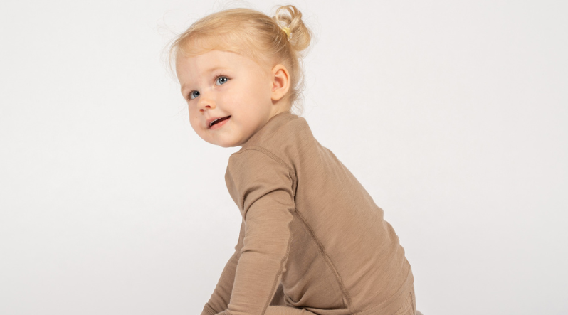 a little baby girl wearing a beige two piece set of merino clothing.