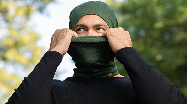 Man outdoors wearing dark green merino wool gaiter and beanie.