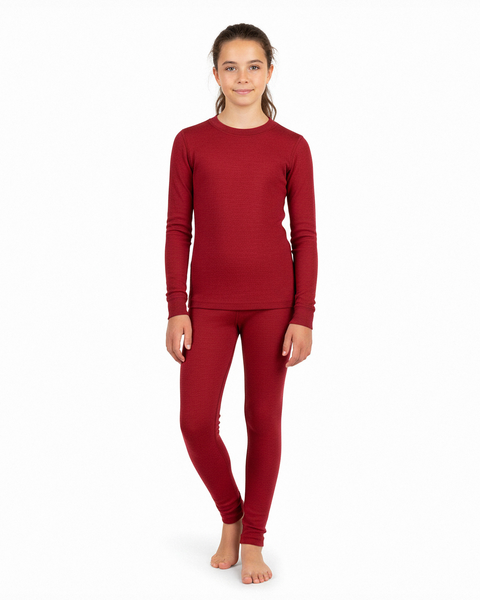 A girl wearing a cherry-red long-sleeve Merino wool base layer top and matching leggings, standing barefoot in a white studio.