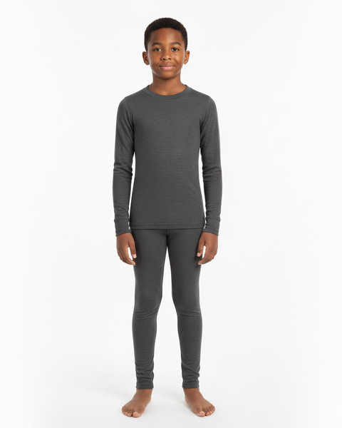 A boy wearing a dark gray long-sleeve Merino wool base layer top and matching leggings, standing barefoot against a white studio background.