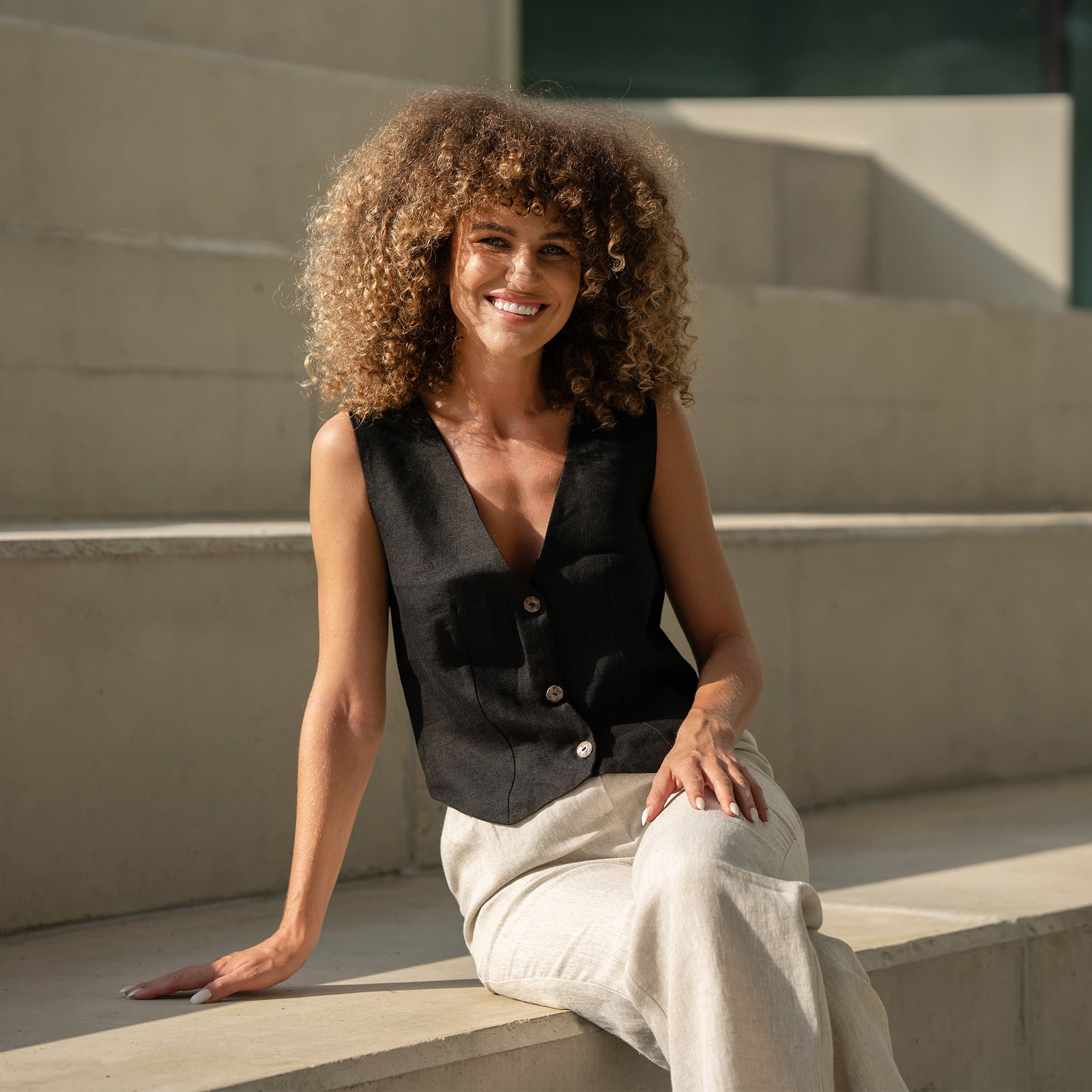 Linen vest ava in black paired with natural color linen pants. Women is walkinkg and smiling