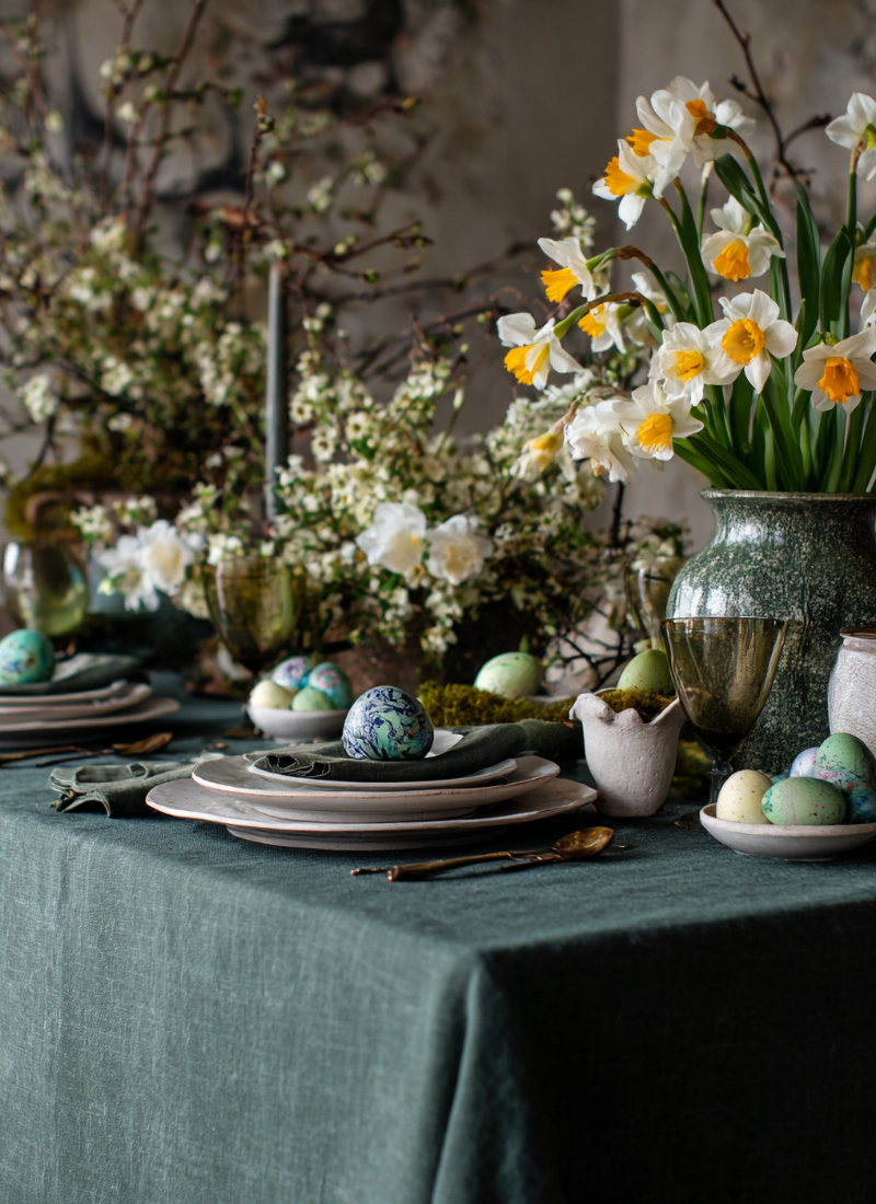 Spring table setting with linen tablecloth, flowers, and decorative eggs.