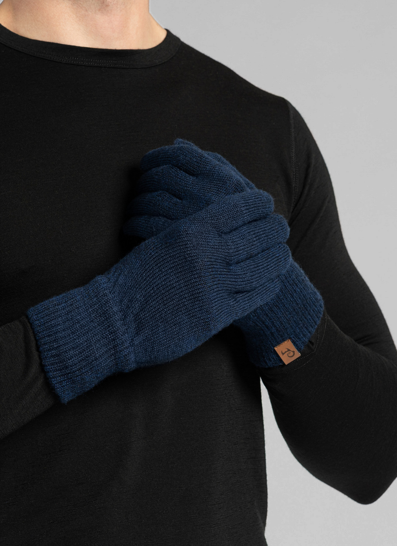 A person wearing a black long-sleeved shirt holds their hands crossed over their chest. They are wearing dark navy blue knitted gloves featuring a small brown logo tag on the cuff.
