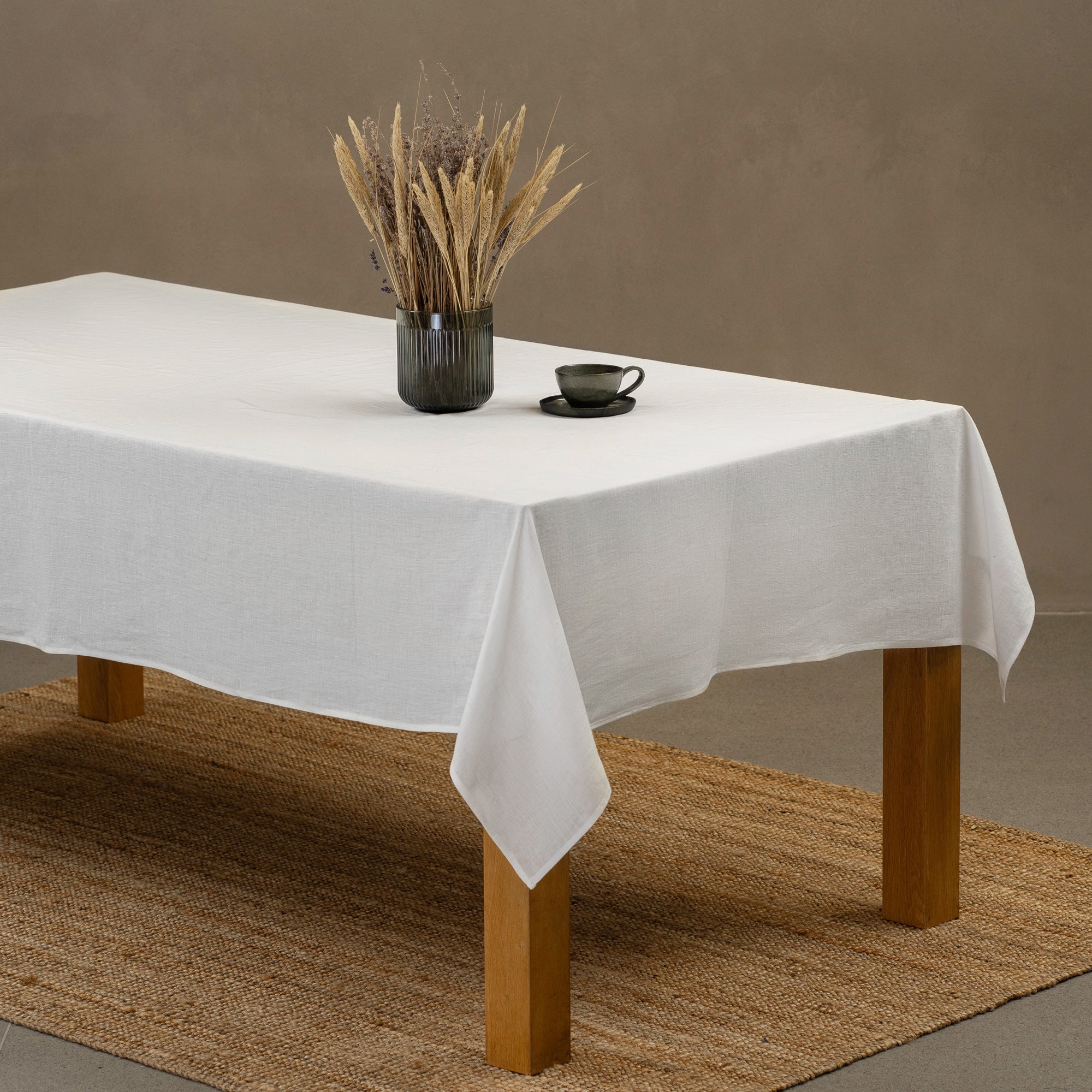 The menique linen tablecloth in dark green color, decorating a Christmas table. there are natural elements, such as pine cones and pine branches on the table top. There is also a wine bottle in a storage bag and candles.