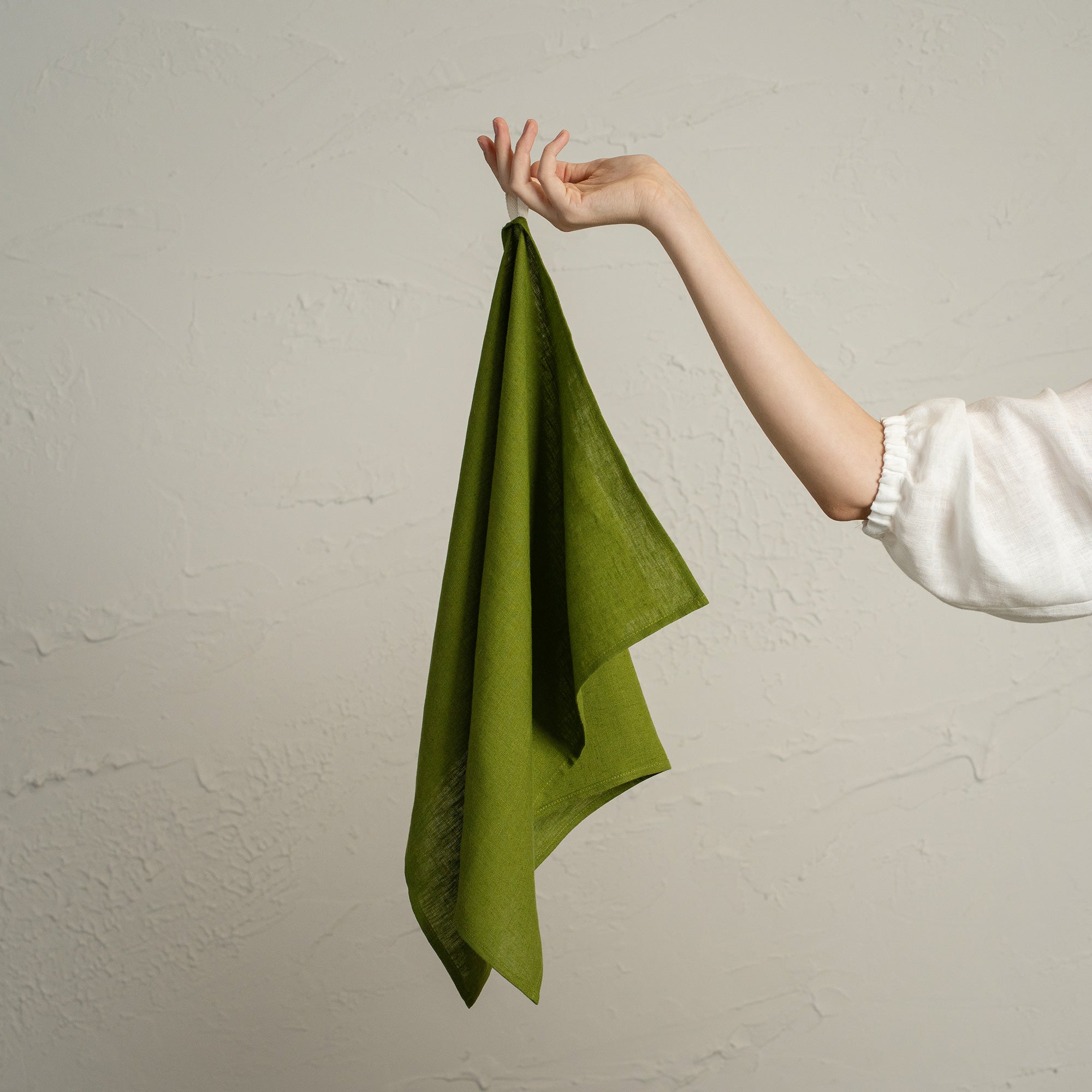 A forest green towel hanging neatly on a wooden peg rack decorated with pinecones, berries, and a small dried orange ornament, against a light textured wall.