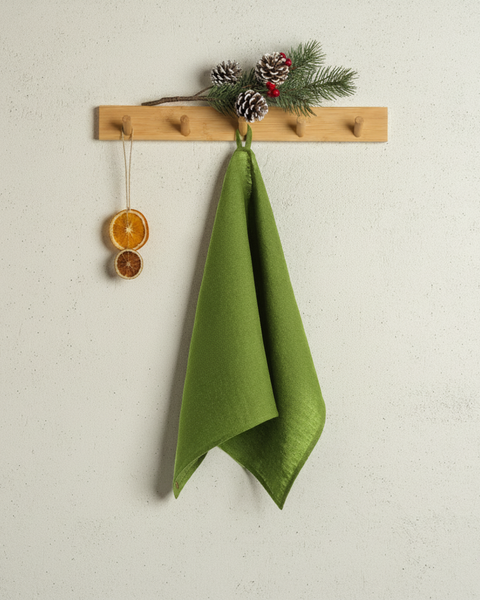 A forest green towel hanging neatly on a wooden peg rack decorated with pinecones, berries, and a small dried orange ornament, against a light textured wall.