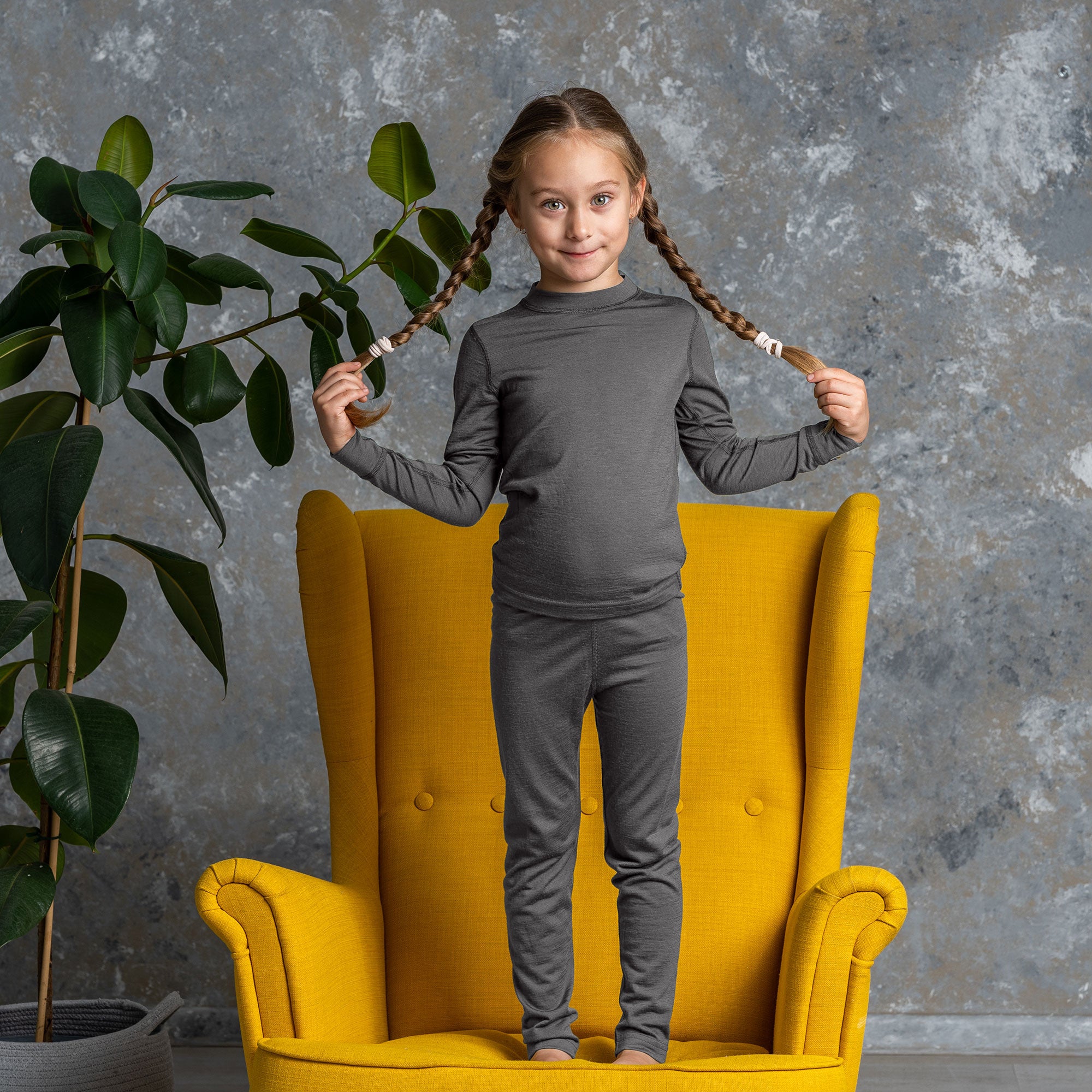 Older boy in gray Merino wool base layer set sitting cross-legged on the floor, neutral background.