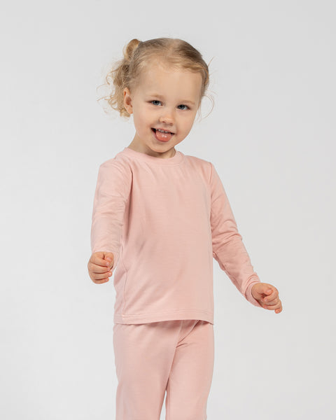 Playful child in pink bamboo long-sleeve top and bottoms, sticking out tongue.
