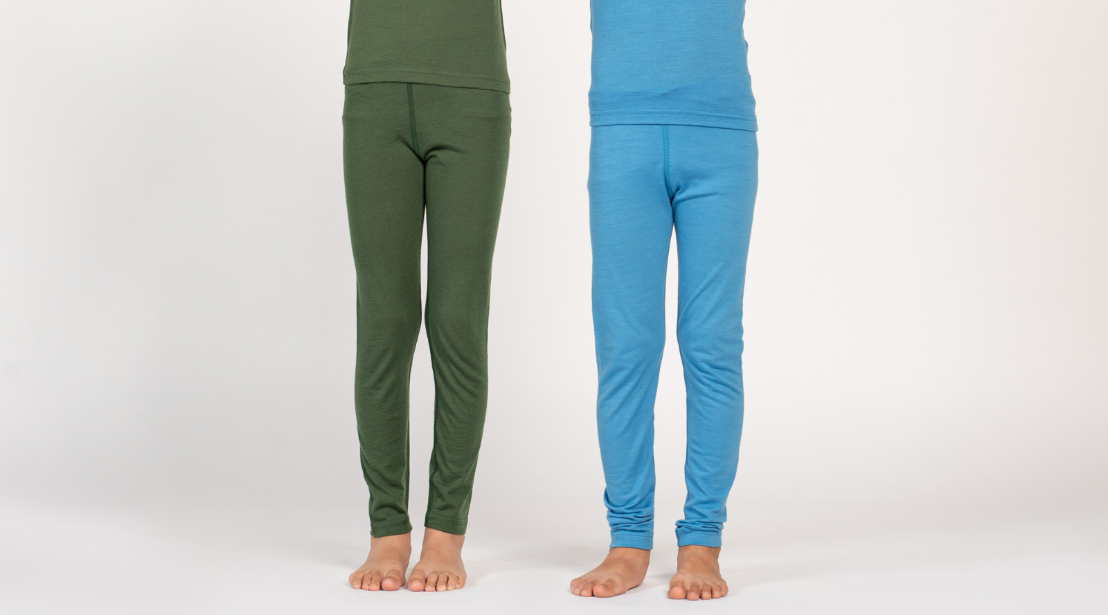 This cropped image shows the legs of two children standing side-by-side against a plain white background. One child is wearing dark green thermal leggings, while the other is wearing a light blue pair.