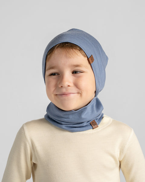 Portrait of a young boy facing forward, wearing a cream t-shirt paired with a matching dusty blue slouchy beanie and neck warmer.
