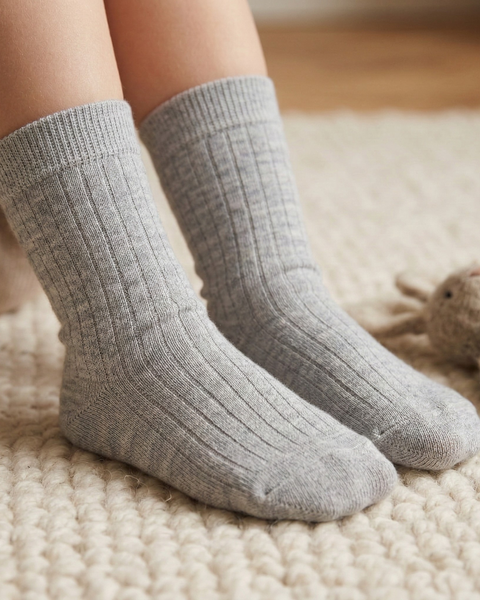 Child wearing light grey merino wool socks on a soft rug.