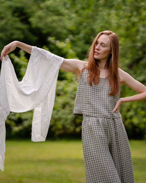 The model is wearing the crop top and culottes matching set in green gingham. She has one of her hands resting on the hip, while the other one is slightly raised, covered with a white linen scarf.