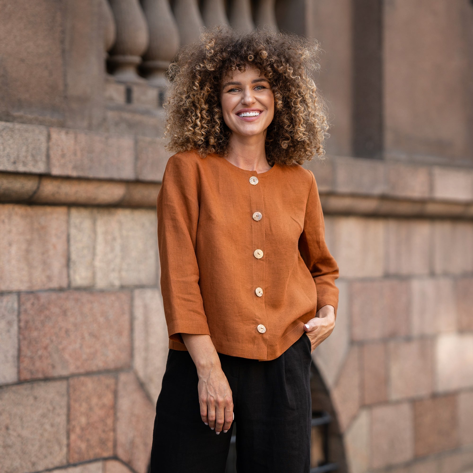 Woman with curly hair wearing almond brown linen jacket Alice and standing in  astreet