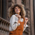 Woman with curly hair standing in a street and wearing Linen Pinafore Jumpsuit Nicci Almond Brown