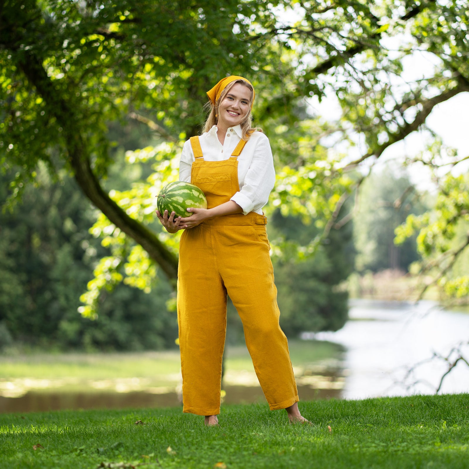Woman in yellow Nicci linen jumpsuit holding a watermelon slice in a park like setting