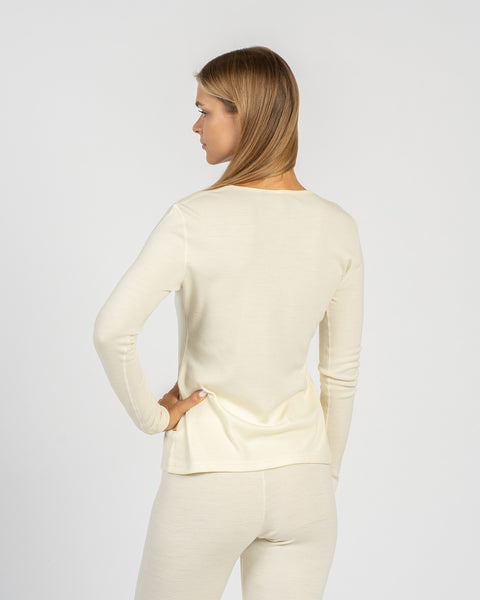 Medium back-view shot of a woman wearing a natural cream-colored, long-sleeve top and leggings, looking over her left shoulder.