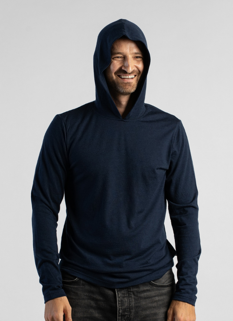 A man wearing a dark navy blue long-sleeve hooded shirt, shown from the waist up against a light gray studio background.