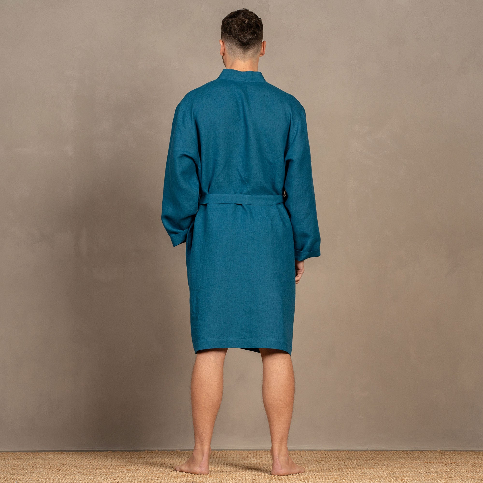 A man wearing the cobalt blue menique linen bathrobe. The bathrobe has pockets on the sides and a tie at the front.