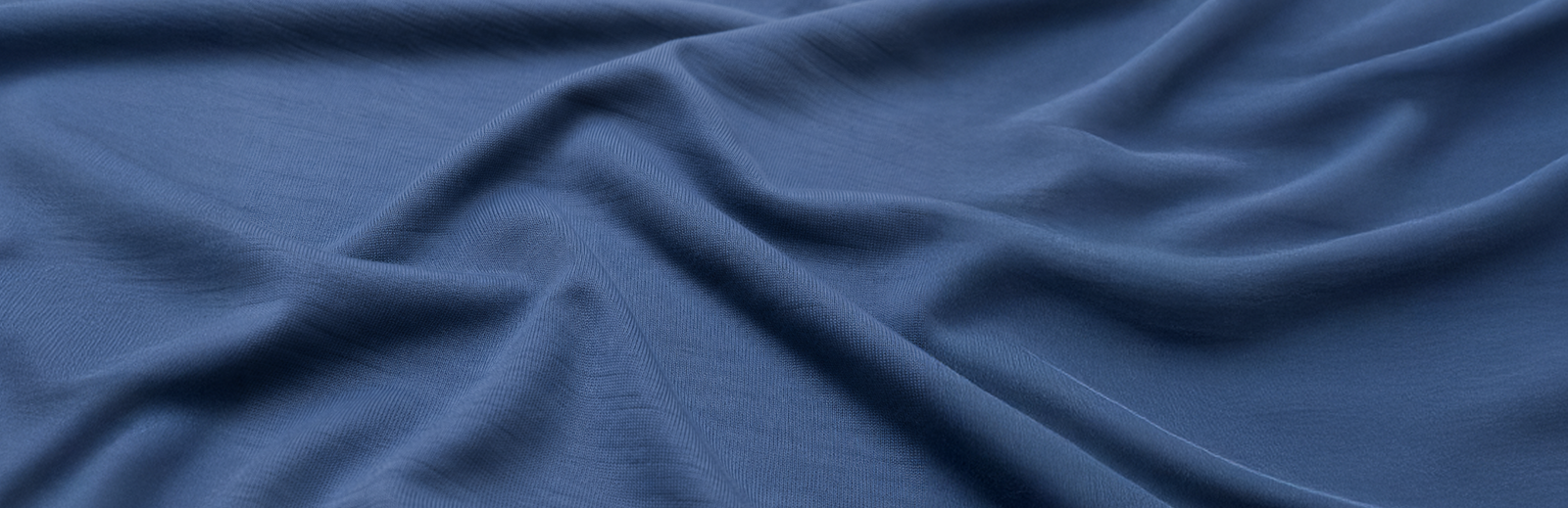 A close-up view of soft, dark blue fabric gently draped to show its smooth texture and rippling folds.