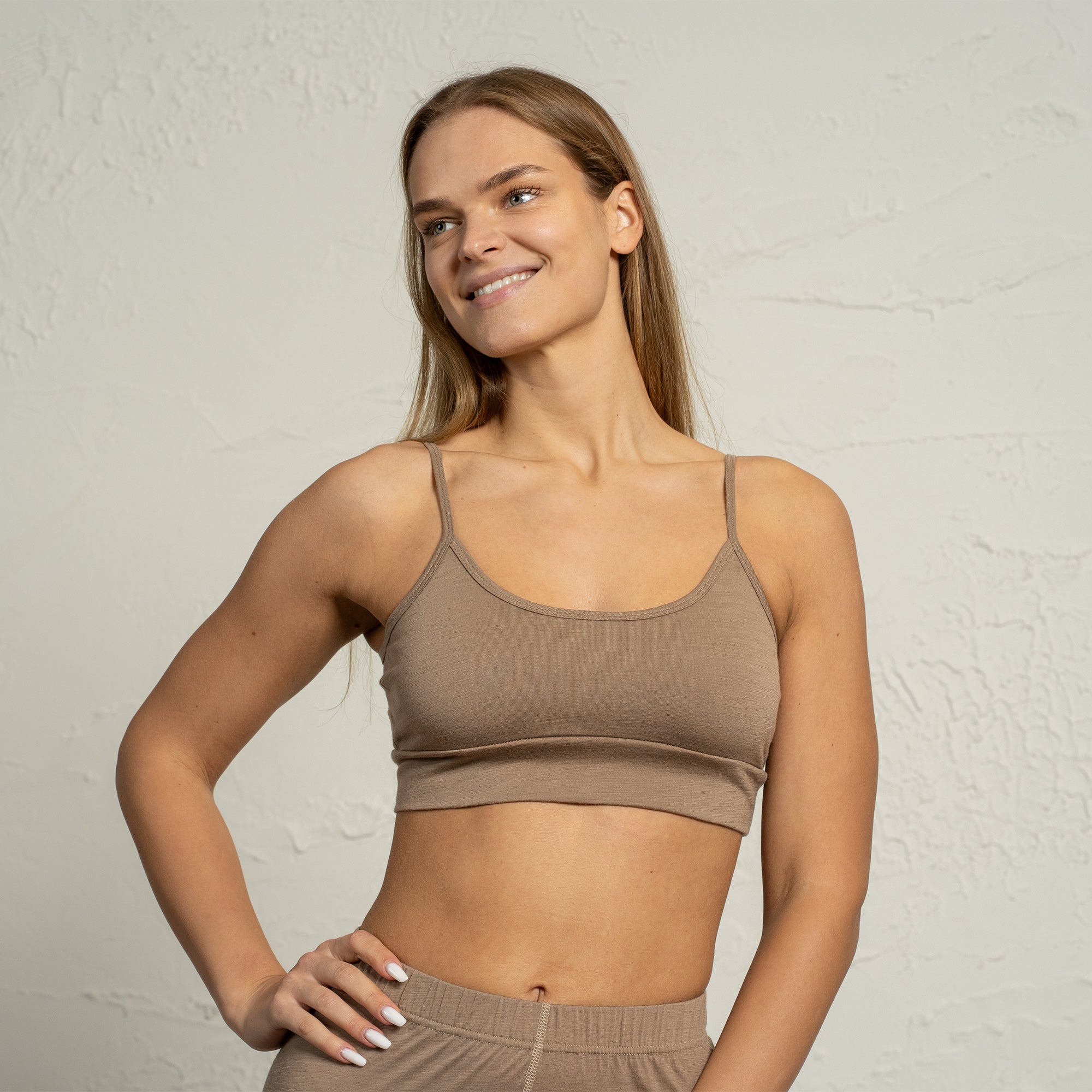 Woman wearing a brown sports bra and blue jeans on a light gray background