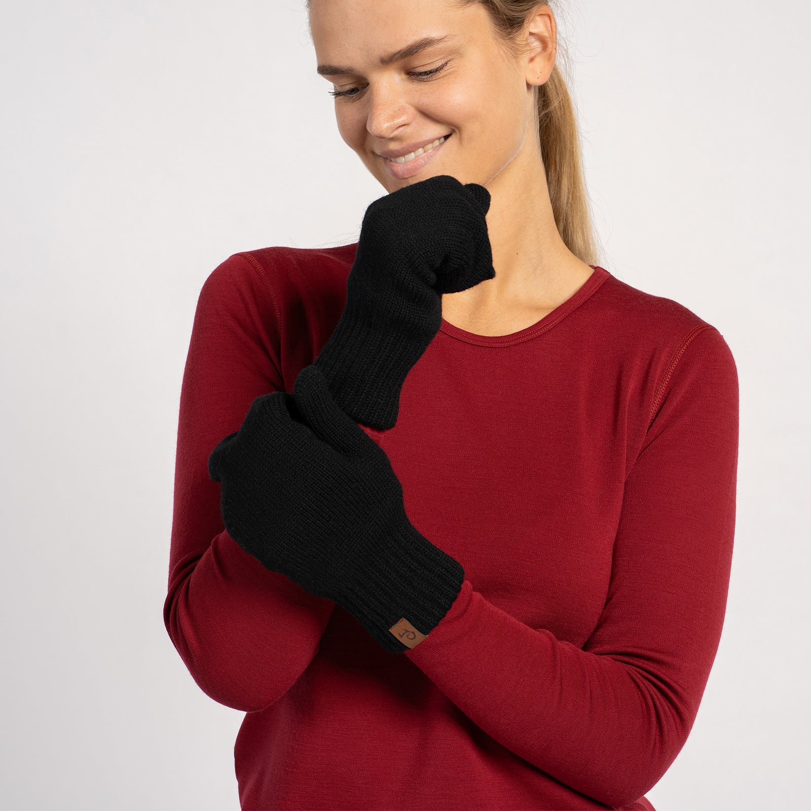 Woman posing in black knitted merino wool mittens with a red long-sleeve top, hand resting on face.