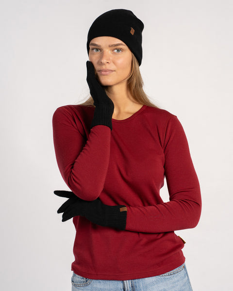 Woman in black cashmere beanie and matching short gloves, front view, hand resting on her face, styled with a royal cherry top.