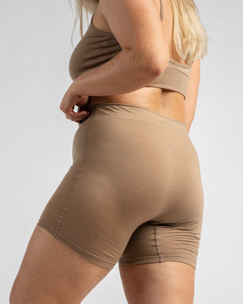 Back three-quarter view of a model wearing a beige sports bra and matching beige biker shorts.