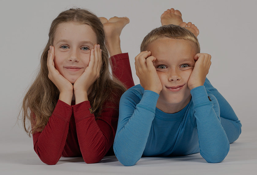 Two children, a girl in a red shirt and a boy in a blue shirt, lying on a gray background with their feet up.