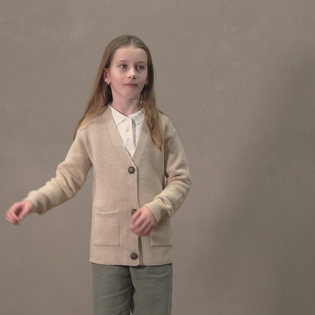 A girl wearing a button front merino wool cardigan in beige color. 