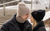 A man and a woman near each other, wearing winter accessories. Both of them are wearing a beanie hat and dickie neck warmer: the woman in black, and the man in creamy beige color.