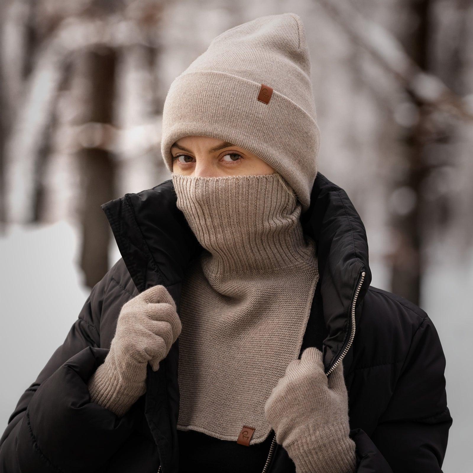 Woman wearing beige merino beanie, neck warmer and gloves, dressed in winter jacket outdoors