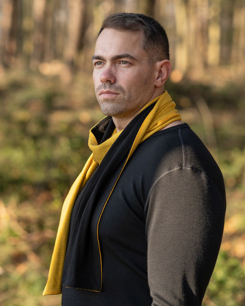 a man wearing the menique Men&#39;s Merino Scarf Power Mango and Black Color mix, in a fall season forest background.