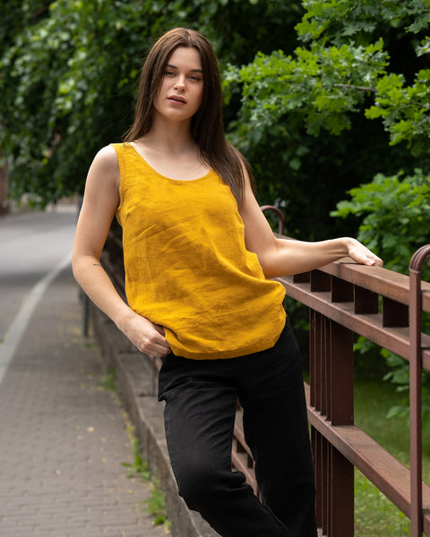 A young woman posing in a city street wearing linen set with a spicy yellow  tank top Hana and pure black linen pants Dakota.